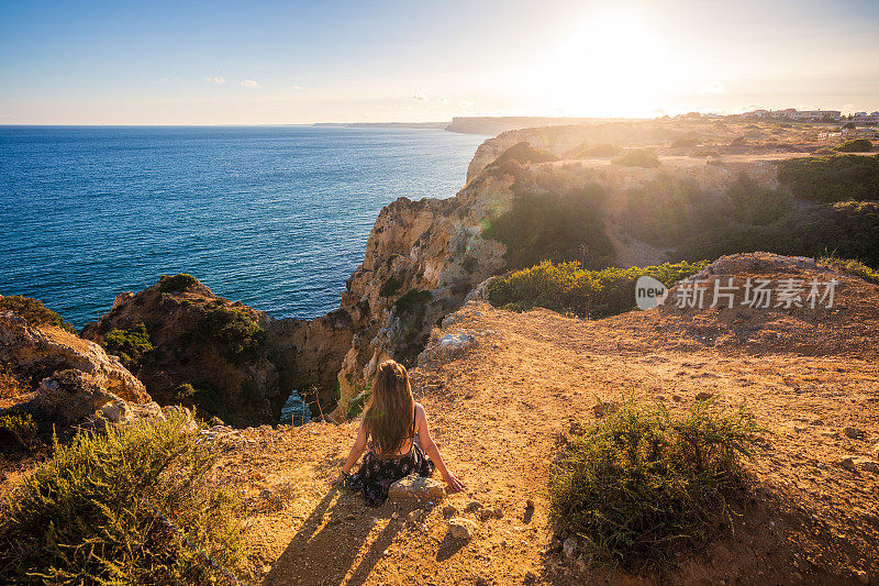 在葡萄牙阿尔加维的Ponta da Piedade悬崖边看日落的女人